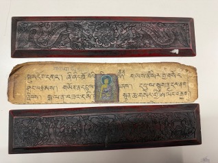 彫刻が施された二つの木製板と中央に古い経文がある紙片の画像